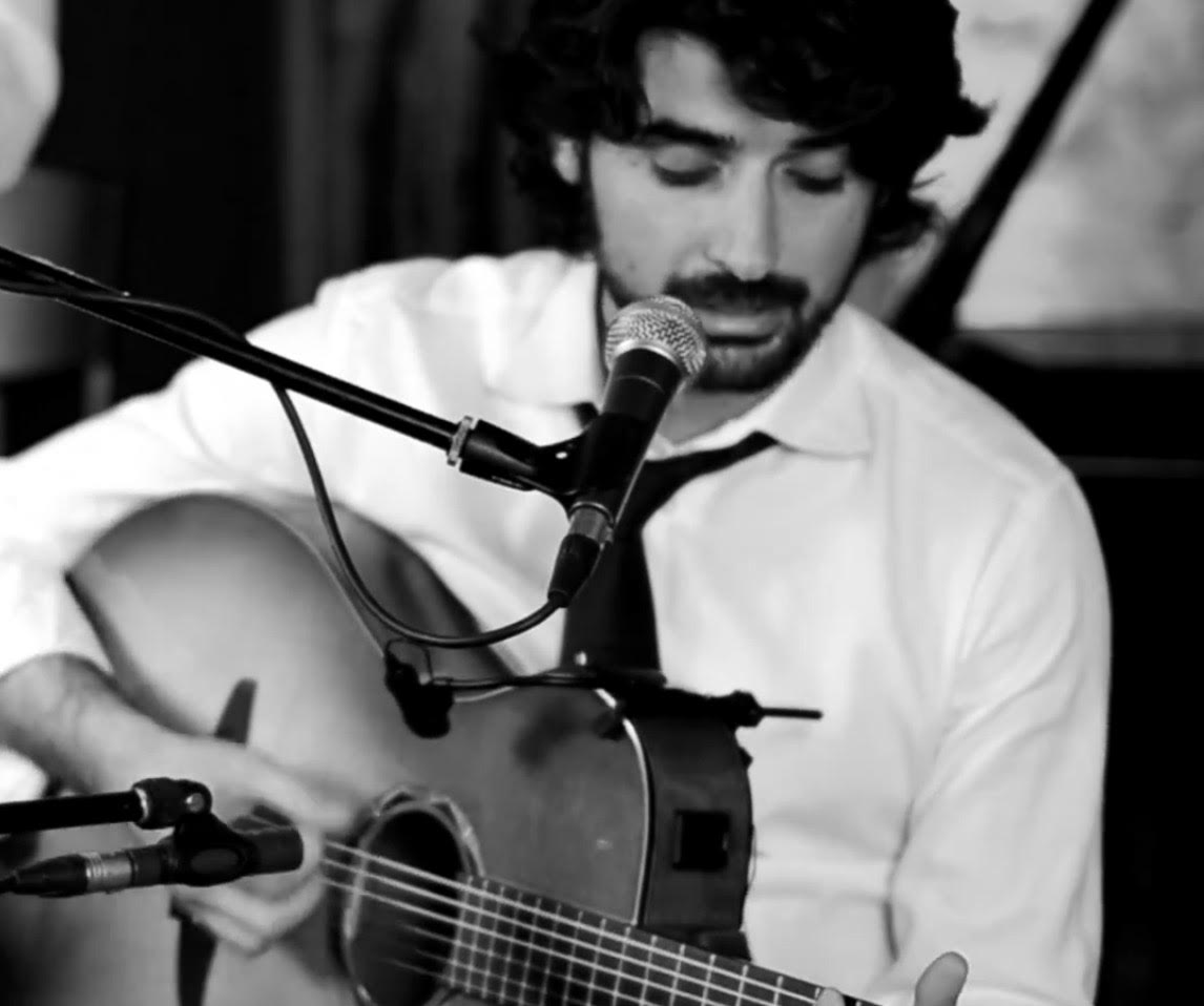 Lorenzo Spini sings into a microphone while playing an acoustic guitar